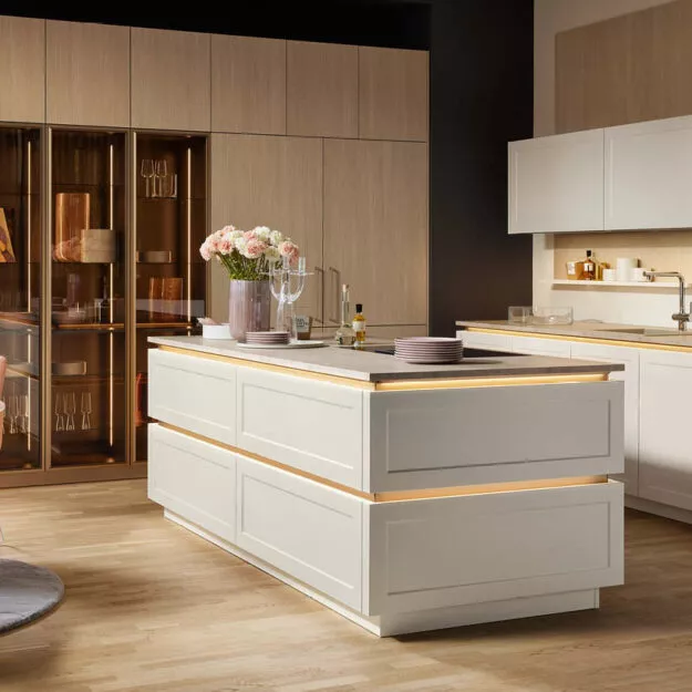 Nolte Küche Ravenna in Magnolia Softmatt mit Kücheninsel und Vitrinenschränken in Sandesche – moderne Designküche von Willemsen Küchen.